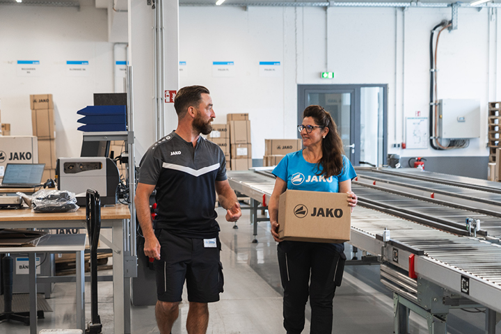 Mitarbeiterin von JAKO vor Rollbändern, auf dem JAKO Kartons laufen