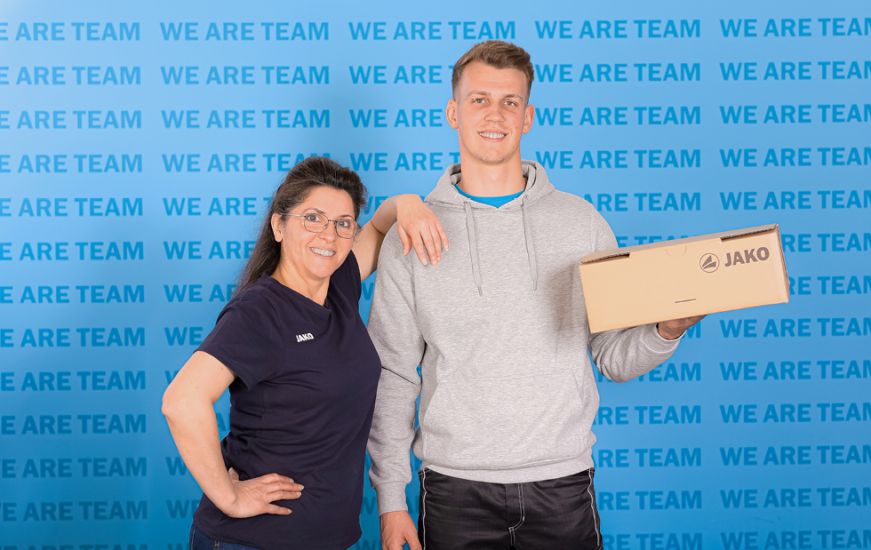 Mitarbeiter von JAKO im Bereich Logistik vor der WE ARE TEAM Wand