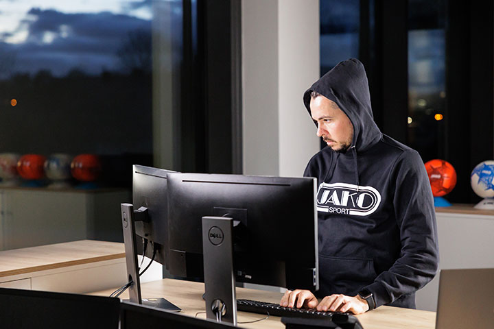 Mitarbeiter von JAKO im Kapuzenpulli vor seinem Monitor