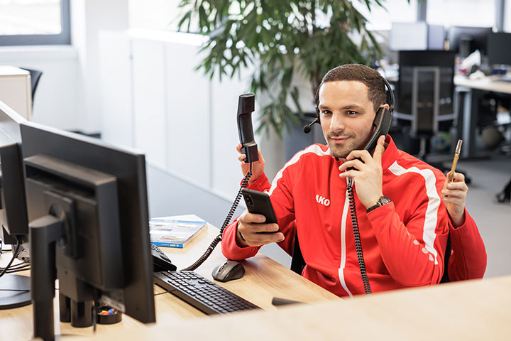 Mitarbeiter von JAKO am Schreibtisch mit Telefonen, Smartphone & Headset