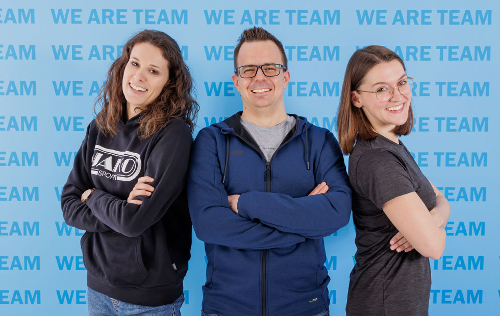Mitarbeiter aus dem Bereich Personal & Finanzen bei JAKO vor der WE ARE TEAM Wand